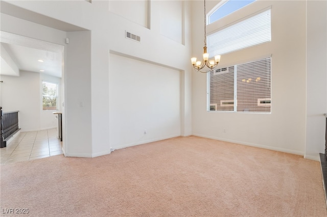 unfurnished room featuring visible vents, a high ceiling, an inviting chandelier, light carpet, and baseboards