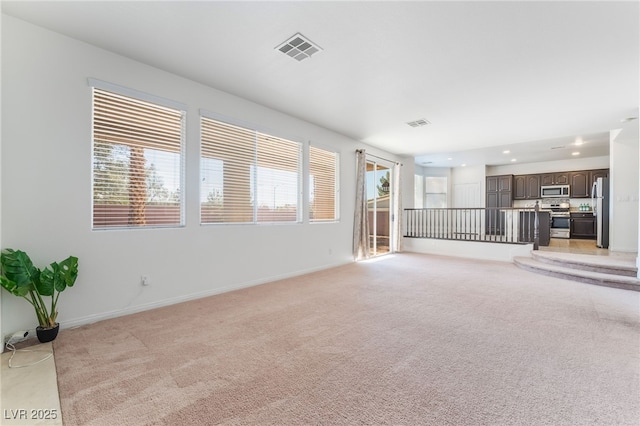 unfurnished living room featuring visible vents, a wealth of natural light, and light colored carpet