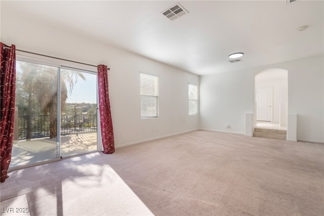 empty room featuring arched walkways, carpet, visible vents, and baseboards