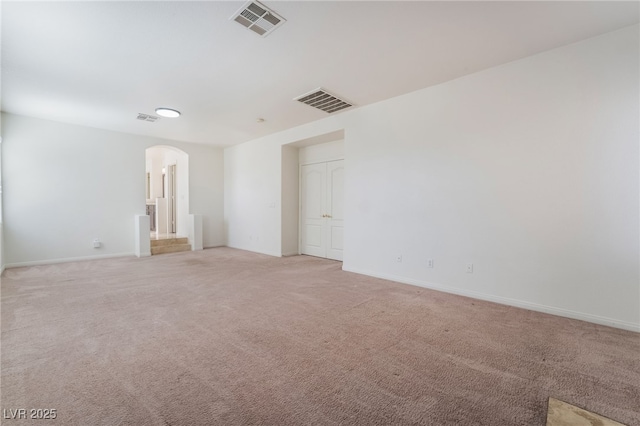 empty room with light carpet, visible vents, arched walkways, and baseboards