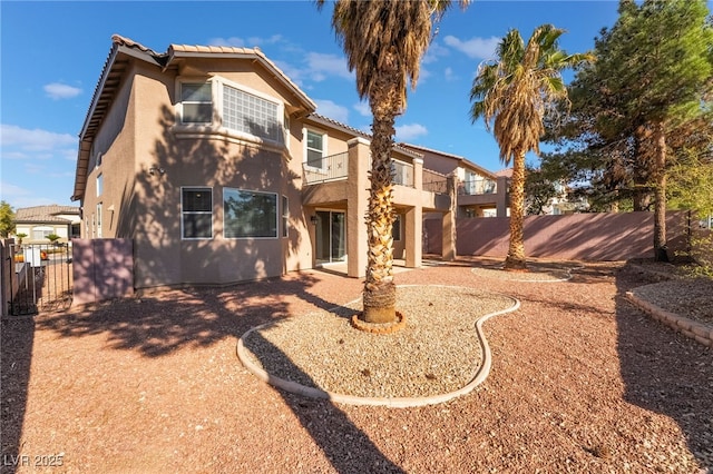 back of house with a tiled roof, fence, a balcony, and stucco siding