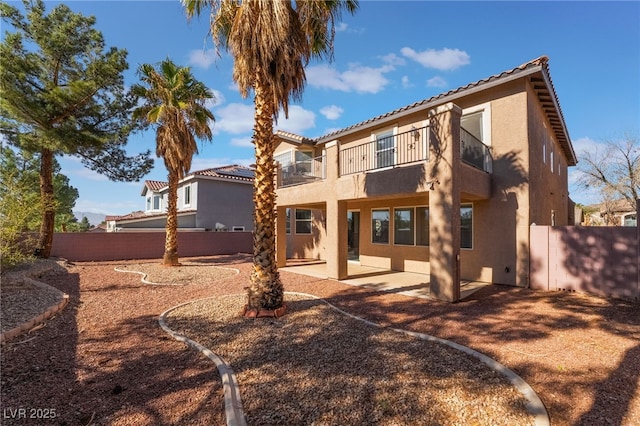 rear view of property featuring stucco siding, a patio, a balcony, and fence