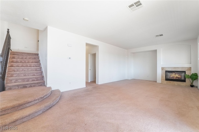 unfurnished living room with stairs, a glass covered fireplace, visible vents, and light colored carpet