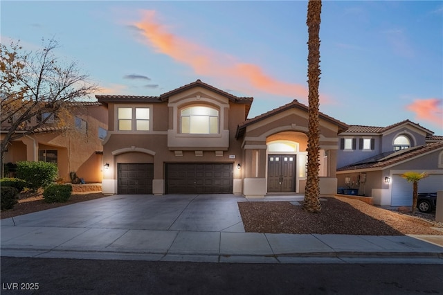 mediterranean / spanish home featuring an attached garage, a tile roof, concrete driveway, and stucco siding