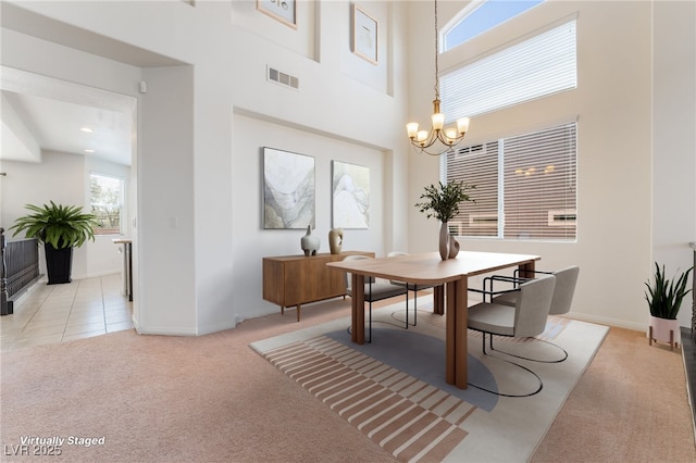 dining space featuring a notable chandelier, light colored carpet, a towering ceiling, baseboards, and visible vents