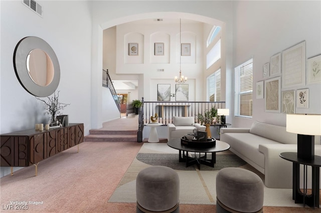 carpeted living area with a towering ceiling, stairs, visible vents, and a notable chandelier