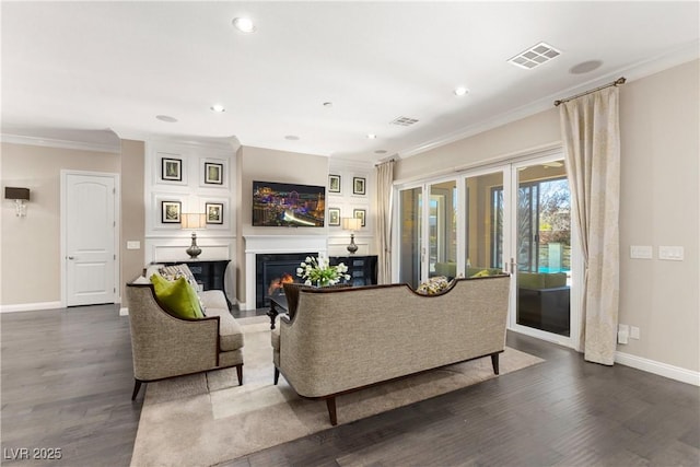 living room featuring visible vents, baseboards, a glass covered fireplace, dark wood-style floors, and ornamental molding