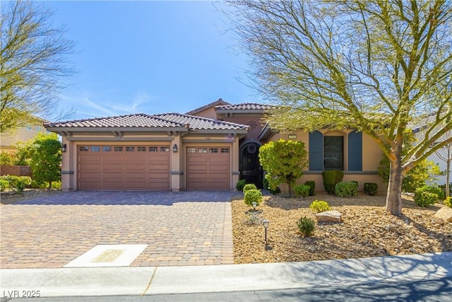 view of front facade featuring decorative driveway, an attached garage, a tile roof, and stucco siding