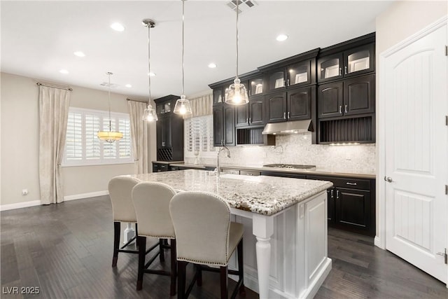 kitchen featuring a breakfast bar, visible vents, backsplash, a sink, and under cabinet range hood