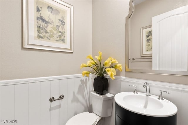 half bathroom with toilet, vanity, and wainscoting