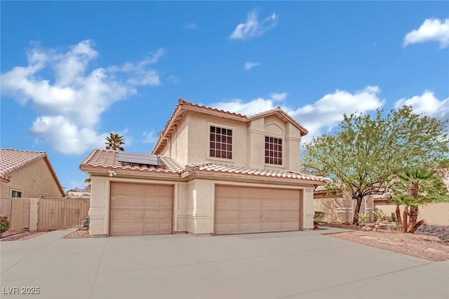 mediterranean / spanish house featuring stucco siding, driveway, a tile roof, fence, and solar panels