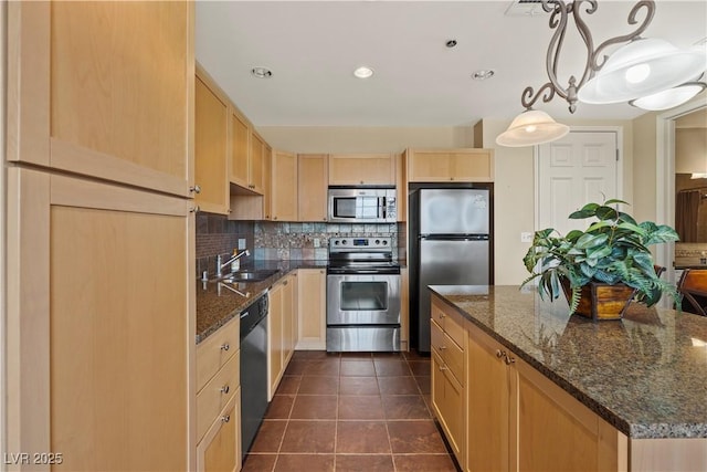 kitchen with a sink, stainless steel appliances, light brown cabinetry, dark tile patterned floors, and backsplash