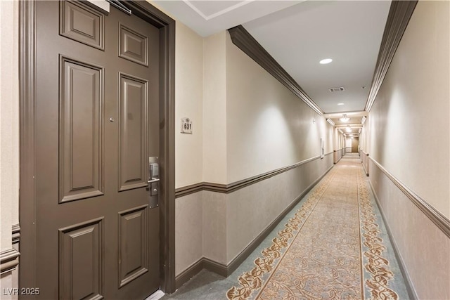 hall with a wainscoted wall, crown molding, recessed lighting, visible vents, and a decorative wall