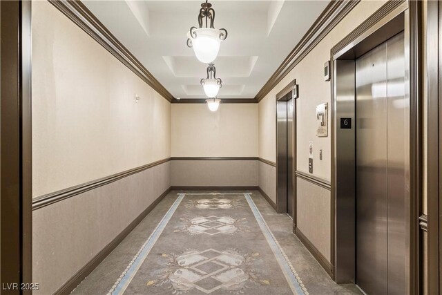 corridor with elevator, concrete floors, a tray ceiling, and ornamental molding