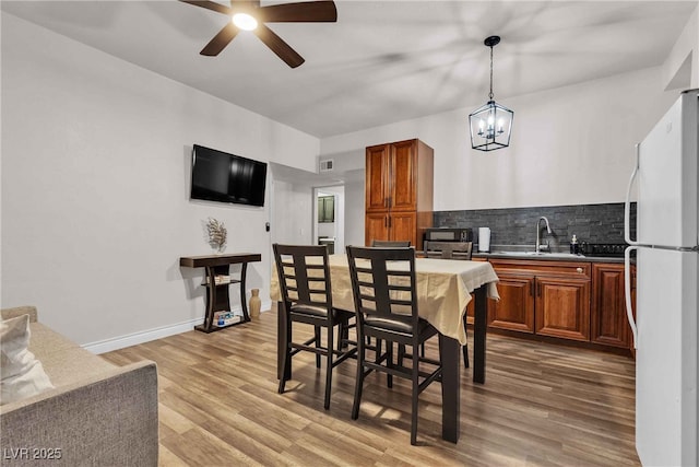 kitchen featuring baseboards, freestanding refrigerator, a sink, light wood-style floors, and backsplash