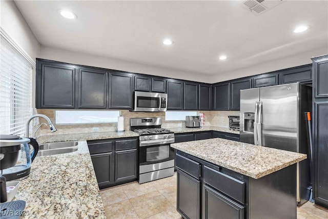 kitchen with visible vents, appliances with stainless steel finishes, a sink, a kitchen island, and light stone countertops