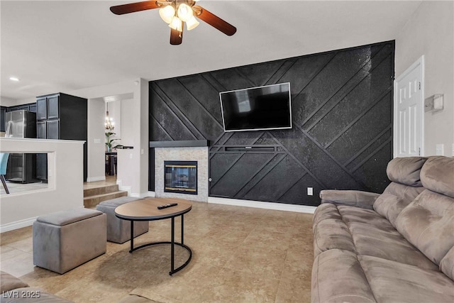 living room featuring an accent wall, a glass covered fireplace, a ceiling fan, and baseboards