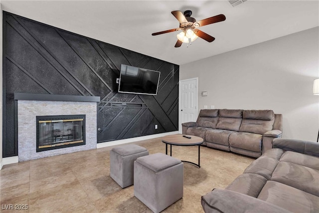 living area featuring an accent wall, a stone fireplace, a ceiling fan, and baseboards