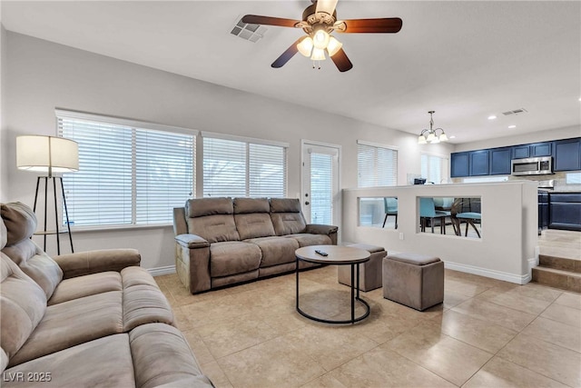 living area with baseboards, ceiling fan with notable chandelier, light tile patterned flooring, and a healthy amount of sunlight