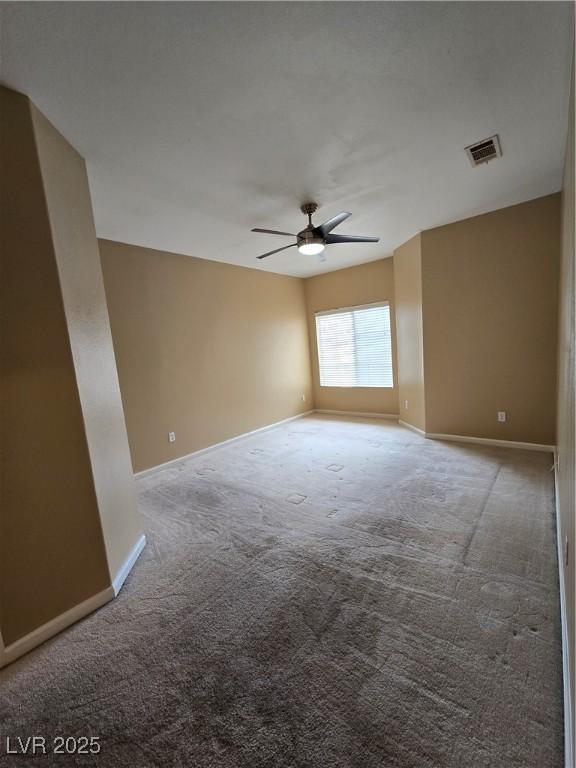 carpeted empty room featuring baseboards, visible vents, and a ceiling fan