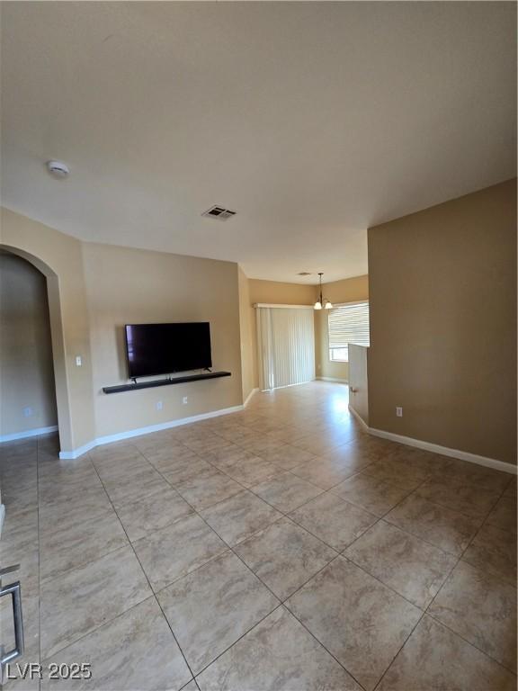 unfurnished living room with arched walkways, tile patterned flooring, visible vents, and baseboards