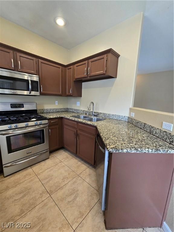 kitchen featuring dark stone counters, appliances with stainless steel finishes, a peninsula, dark brown cabinets, and a sink