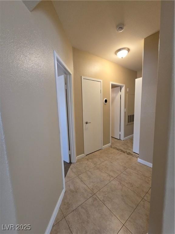 hall with visible vents, baseboards, and light tile patterned floors