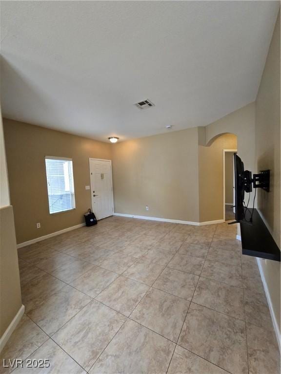 unfurnished room featuring arched walkways, light tile patterned floors, visible vents, and baseboards