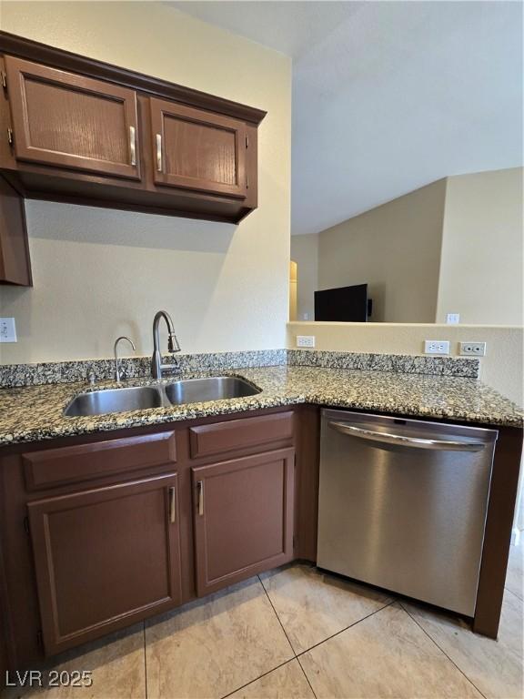 kitchen featuring dark brown cabinetry, a peninsula, dark stone counters, a sink, and dishwasher