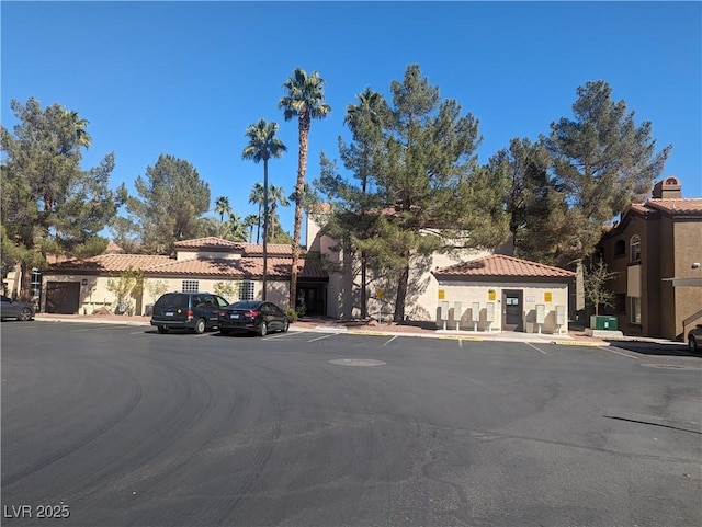 view of front facade with stucco siding, uncovered parking, and a tiled roof