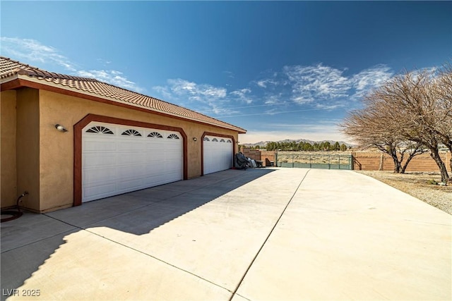 view of side of property featuring a garage, fence, a tiled roof, driveway, and stucco siding