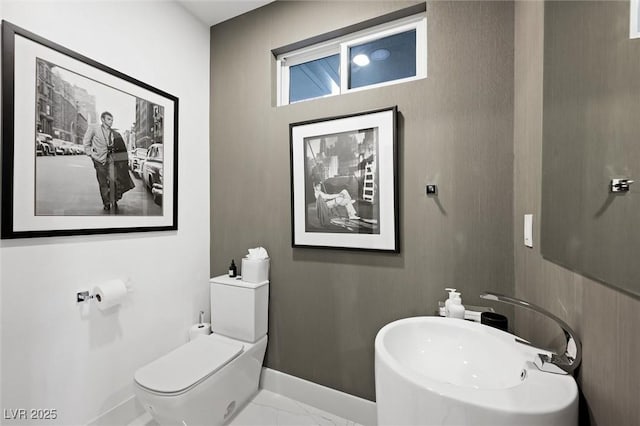 half bath with marble finish floor, a sink, toilet, and baseboards