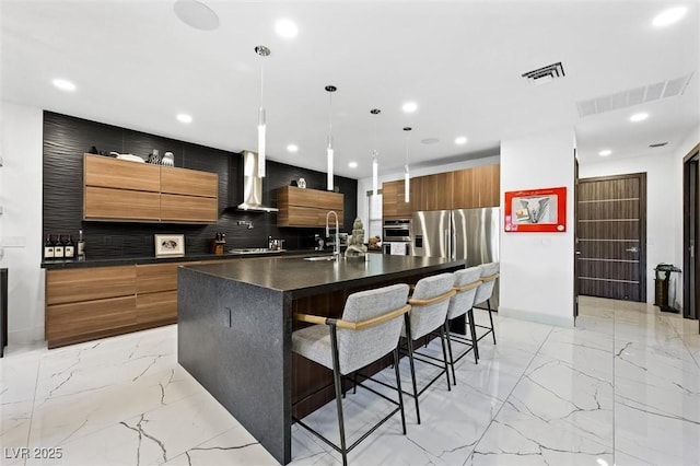 kitchen featuring dark countertops, marble finish floor, wall chimney range hood, and modern cabinets