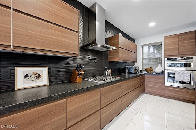 kitchen with wall chimney exhaust hood, modern cabinets, appliances with stainless steel finishes, marble finish floor, and backsplash