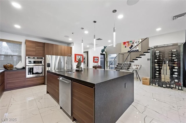 kitchen with marble finish floor, a center island with sink, stainless steel appliances, dark countertops, and modern cabinets