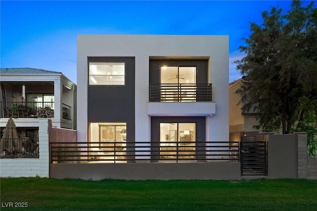 rear view of property featuring a balcony, a lawn, and stucco siding