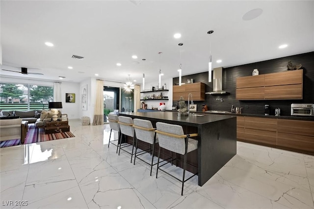 kitchen featuring marble finish floor, dark countertops, brown cabinetry, wall chimney range hood, and modern cabinets