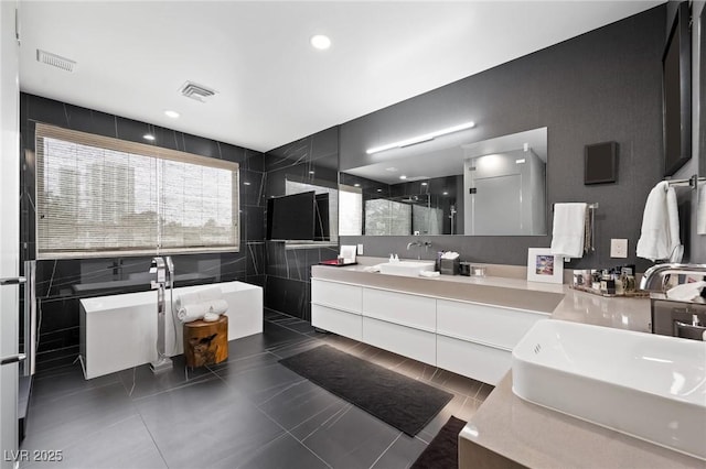 bathroom with double vanity, a stall shower, visible vents, a sink, and tile walls