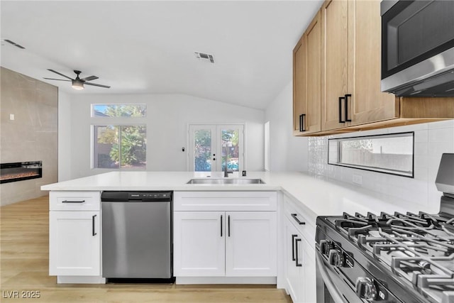 kitchen with a tile fireplace, a peninsula, light countertops, stainless steel appliances, and a sink