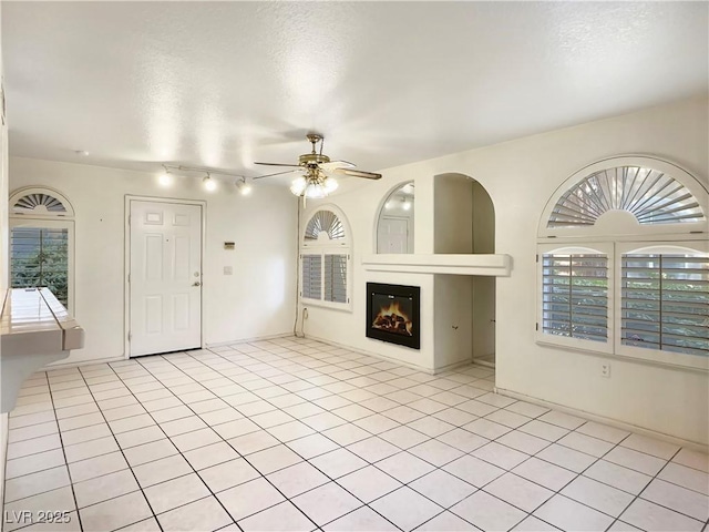 unfurnished living room featuring a glass covered fireplace, ceiling fan, a textured ceiling, and light tile patterned floors