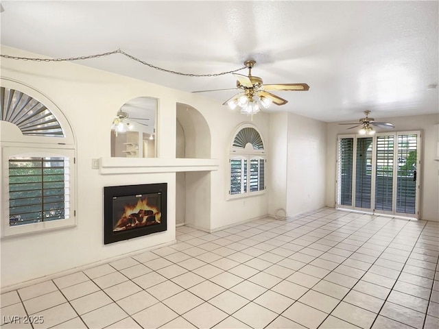 unfurnished living room with ceiling fan, a glass covered fireplace, and tile patterned floors