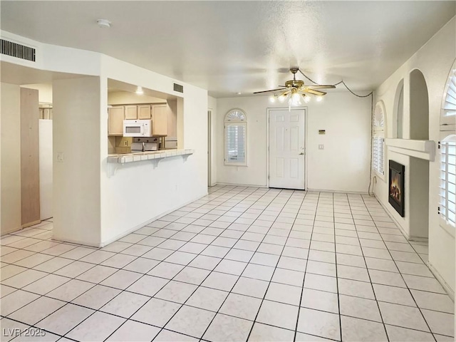 unfurnished living room featuring light tile patterned floors, ceiling fan, visible vents, and a glass covered fireplace