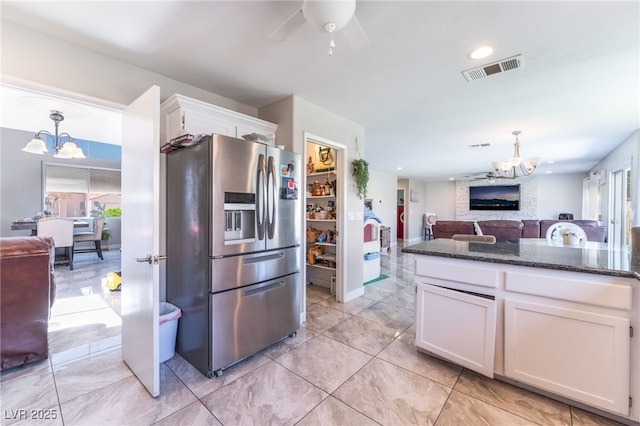 kitchen featuring stainless steel refrigerator with ice dispenser, visible vents, open floor plan, white cabinets, and dark stone counters