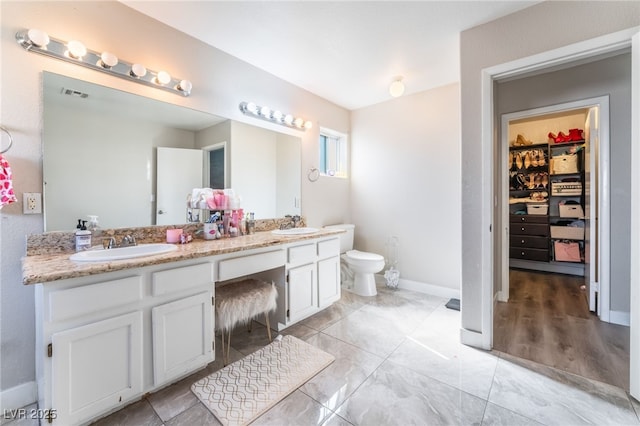 bathroom featuring double vanity, visible vents, a walk in closet, and a sink