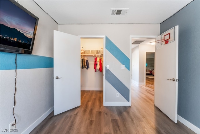 bedroom featuring baseboards, visible vents, wood finished floors, a walk in closet, and a closet