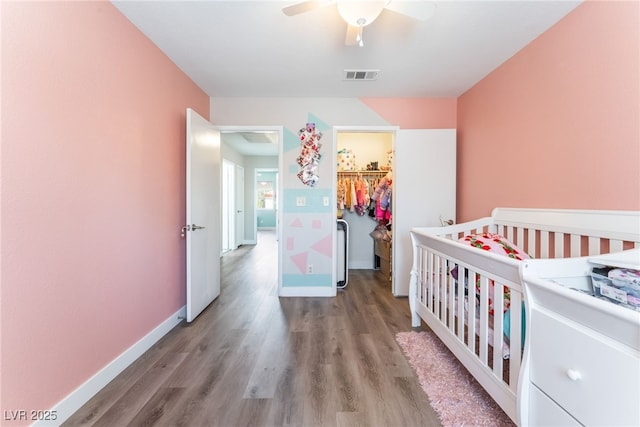 bedroom with wood finished floors, visible vents, baseboards, a closet, and a walk in closet