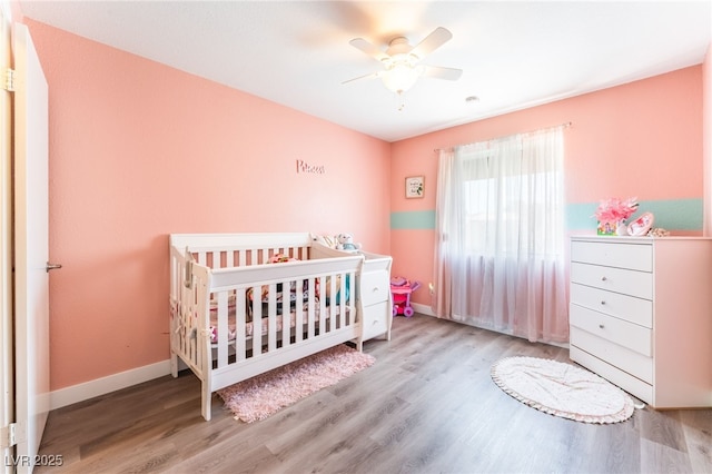 bedroom featuring ceiling fan, a crib, baseboards, and wood finished floors