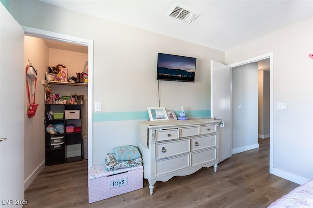 bedroom featuring baseboards, visible vents, a walk in closet, and wood finished floors