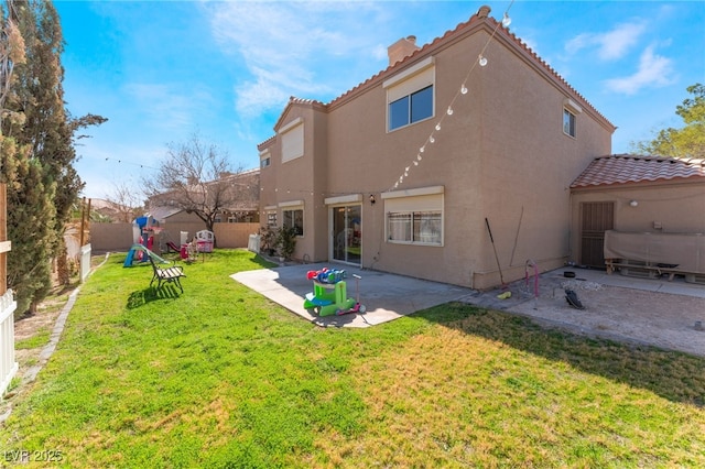 back of property with a fenced backyard, a tiled roof, a yard, a patio area, and stucco siding