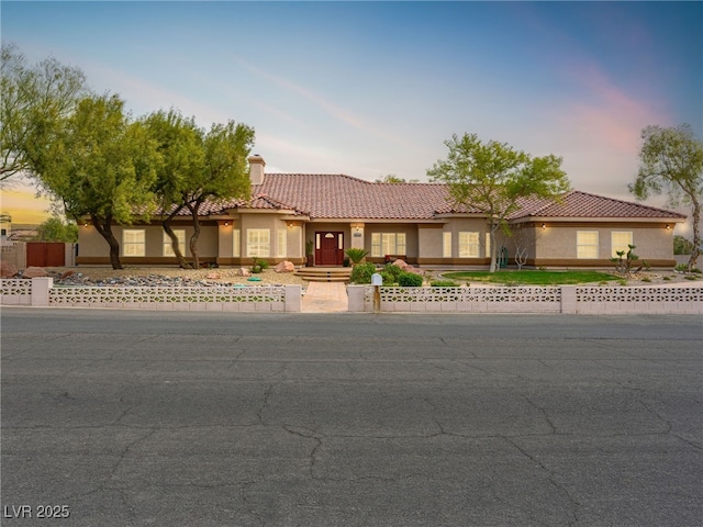 view of front of home with stucco siding, a fenced front yard, a chimney, and a tiled roof